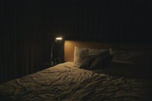 Dark, quiet bedroom prepared for a Better ZZZ's sleep ritual, with a bedside lamp and bed
