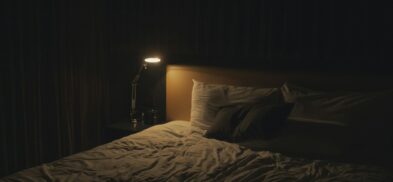 Dark, quiet bedroom prepared for a Better ZZZ's sleep ritual, with a bedside lamp and bed